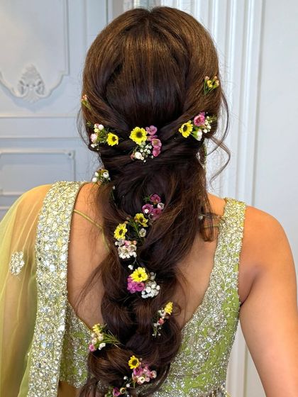 A messy, romantic fishtail braid interwoven with a variety of colorful winter flowers, perfect for a bohemian Mehandi look.