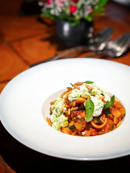 A bowl of fresh pasta with ricotta and vegetables, served at a fine dining restaurant. The focus on the dish with the blurred restaurant background creates an intimate and upscale dining feel.