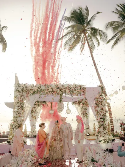 A breathtaking moment as pink smoke fills the air, celebrating the union of a beautiful couple under a floral mandap at their Juhu beach wedding. This is the kind of magic I live to capture.