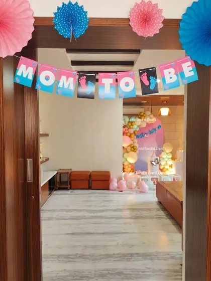 A 'Mom to Be' banner and paper fan decorations, creating a simple and sweet entrance to a baby shower.