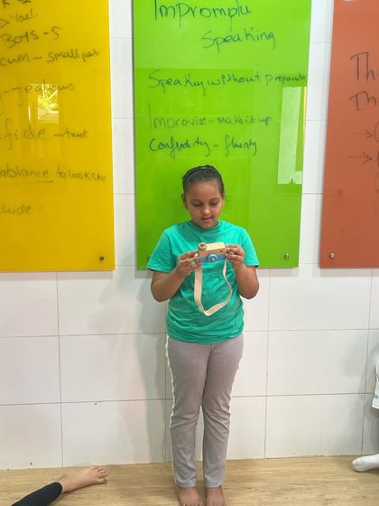 This student uses a toy camera to inspire her impromptu speech. This activity is a cornerstone of our curriculum, designed to build confidence and help students become comfortable speaking spontaneously.