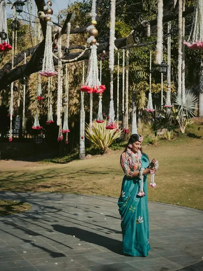 A serene portrait of the bride amidst the beautiful outdoor decor of her Haldi ceremony, holding a floral garland and taking in the moment.