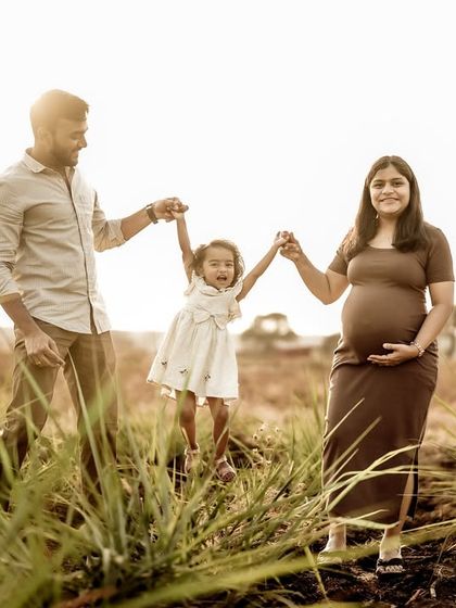 A fun and energetic family moment. The parents swing their daughter between them as they walk through the field, a picture of pure, happy family life.