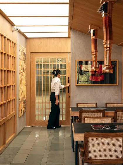 A staff member moves through the space, highlighting the functional flow of the design. The wooden lattice screens and paneled doors create a sense of rhythm and order, guiding movement through the restaurant.