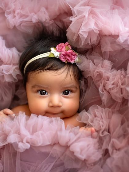 Surrounded by soft pink tulle, this little one looks like a flower herself. This is a beautiful example of a creative setup for a 4-month-old baby girl.