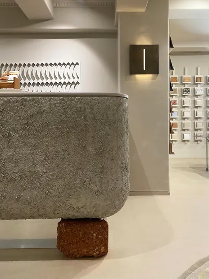 The reception counter at the JOSMO store is a statement piece, combining a rough, textured concrete finish with a raw laterite stone base. This juxtaposition of industrial and earthy materials creates a powerful first impression.