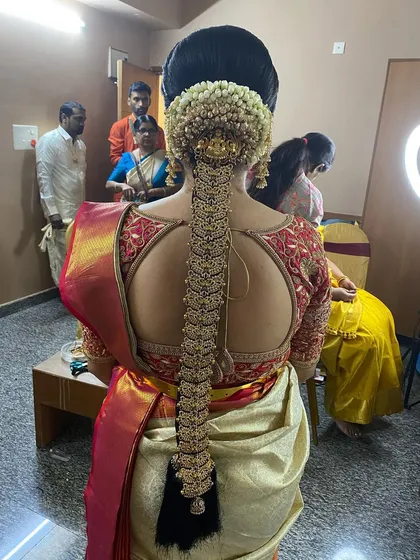 This behind-the-scenes shot shows the final placement of the temple jewellery on a traditional Muhurtham braid. The ring light in the background highlights the shine and detail of the hairstyle.