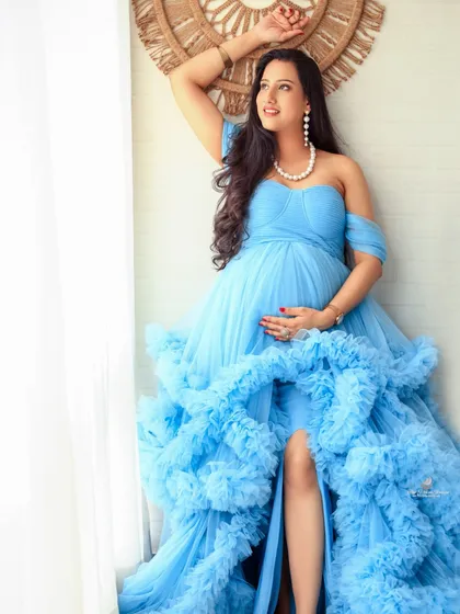 A stunning window-lit portrait. The natural light beautifully illuminates the mom-to-be's profile and the flowing silhouette of her blue gown, creating a soft and timeless look.