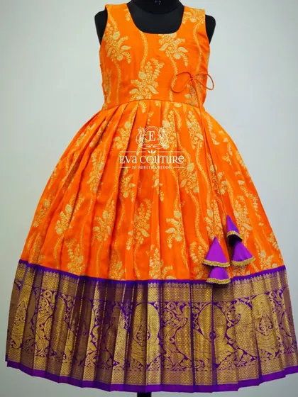 A sleeveless orange brocade frock with a rich purple Kanchi Pattu border. A bright and cheerful outfit for any celebration.