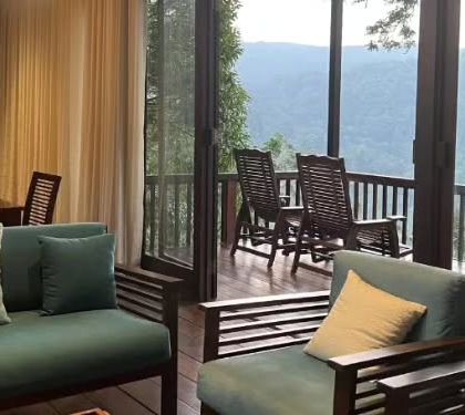 The living room of a villa in Coorg opens up to a balcony with rocking chairs, perfect for enjoying the misty valley views.