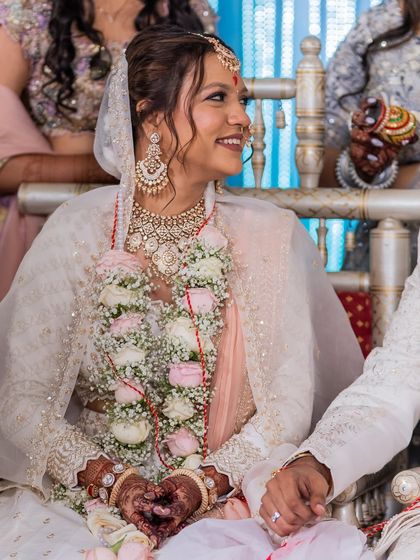 A close-up of the bride's joyful expression, wearing a beautiful white lehenga and floral garlands.