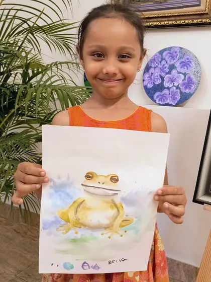 This young artist smiles as she shows off her beautifully rendered watercolor frog, complete with subtle color blending.