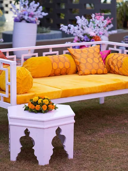 Modern seating for a Haldi ceremony. This white bench with vibrant yellow cushions offers a comfortable and stylish alternative to traditional seating.