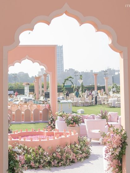 A view through the peach-colored arches, revealing the sprawling lawn setup with a water feature and multiple seating areas.