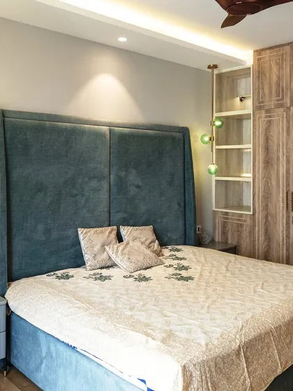 This bedroom is a perfect blend of comfort and style. A tall, upholstered headboard in a deep teal provides a sense of grandeur, while the green glass pendant lights add a pop of color and modern flair.