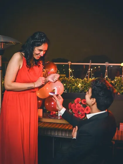 The magical moment of a surprise proposal, with the groom on one knee and a beautifully decorated table with roses and balloons.