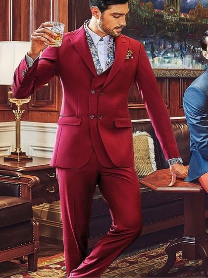 This shot from the SPAADAA 2021 campaign highlights a bold approach to formalwear. The vibrant red three-piece suit, paired with a patterned shirt, is styled to convey confidence and modern elegance in a classic setting.