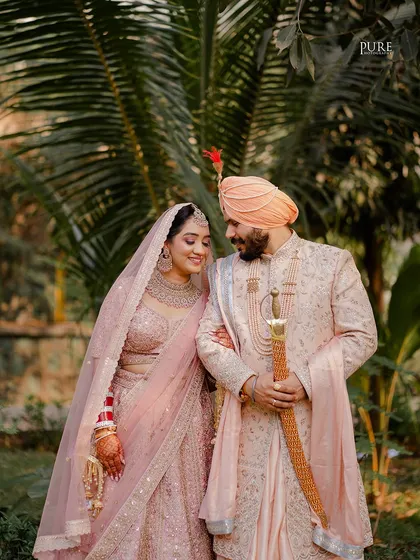 A classic portrait showcasing the regal attire of a Sikh couple. The groom holds his kirpan, a symbol of his duty to protect, as they stand together.