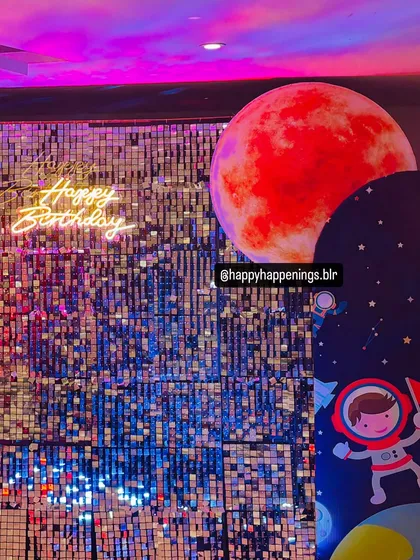 A close-up of the shimmering silver sequin backdrop with a red planet prop and a "Happy Birthday" neon sign. This combination of textures and light creates a dynamic and visually interesting focal point.