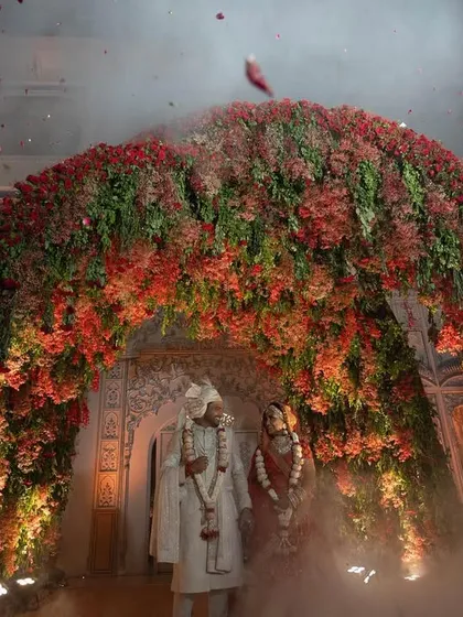 The couple framed by a massive floral arch, with smoke effects adding a touch of drama and magic to their Varmala ceremony.
