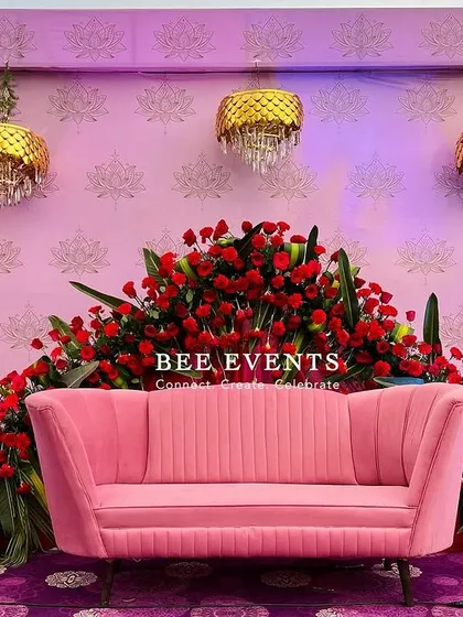 A bold and beautiful stage setup featuring a striking combination of red roses and a pink sofa against a lavender backdrop. The golden arch windows and hanging chandeliers add a touch of royal flair.