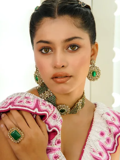A close-up beauty shot showcasing glossy lips and defined eyes, paired with stunning green jewelry.