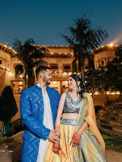 A lovely evening portrait of the couple at their Mehendi, the lit-up palace behind them adding to the romantic atmosphere.