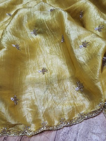 A beautiful crush tissue saree in a mustard yellow shade. The light-as-air fabric is adorned with small, sparkling embroidery, making it a comfortable yet festive option.
