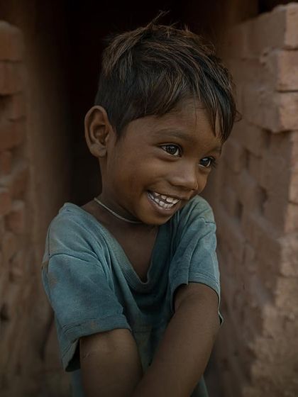 A candid portrait of a young boy at a brick kiln, his shy but genuine smile offering a moment of light and happiness in a harsh environment.