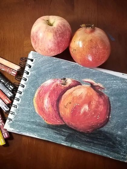 A still life study of fruits next to the real thing. Using oil pastels, the student captured the colours and shapes of the apple and pomegranate perfectly.