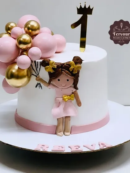 A first birthday cake for a little girl holding a bouquet of balloons. This chocolate mousse cake has a simple, elegant design with pink and gold accents.