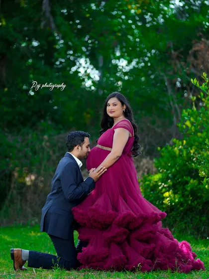 A tender moment with the father-to-be kissing the baby bump. The mother-to-be is wearing a wine-colored ruffled gown in a beautiful outdoor setting.