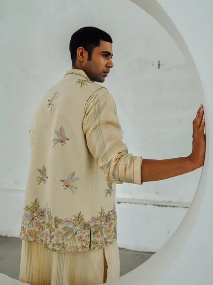 A lookbook image for Wabi Sabi, showcasing a men's bundi jacket with delicate bird embroidery. The circular architectural element frames the model and adds a modern touch.