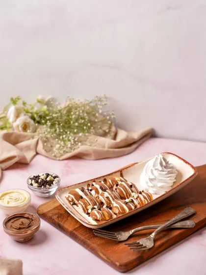 Mini pancakes drizzled with chocolate sauce, styled on a wooden board with dipping sauces. This clean and bright setup is ideal for a cafe menu or a food delivery app.