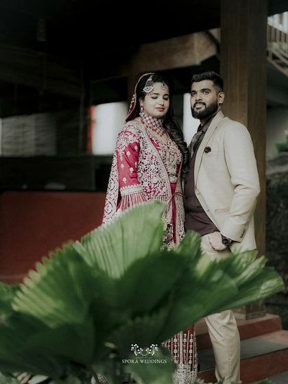 The couple posing with a large palm leaf in the foreground, adding a tropical and artistic element to their portrait.