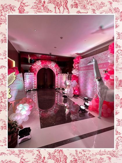 The full entrance area for the pink baby shower, showing the illuminated archway, welcome signs, and a large white giraffe prop, creating an immersive and luxurious experience.