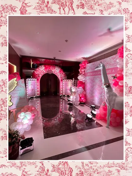 The full entrance area for the pink baby shower, showing the illuminated archway, welcome signs, and a large white giraffe prop, creating an immersive and luxurious experience.
