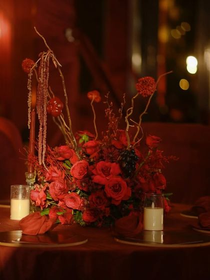 A stunning centerpiece combining red roses, dried branches, and grapes. The varied textures and shades of red add depth and sophistication to the arrangement.