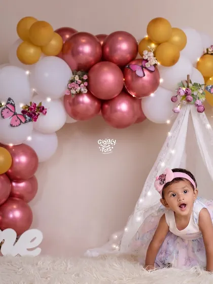 A little girl peeks out of her butterfly-themed tent, surprised and delighted by the beautiful setup for her first birthday.
