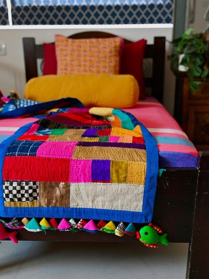 A close-up of the vibrant patchwork on the improv quilt. The mix of silks, cottons, and prints creates a rich tapestry of color and texture.