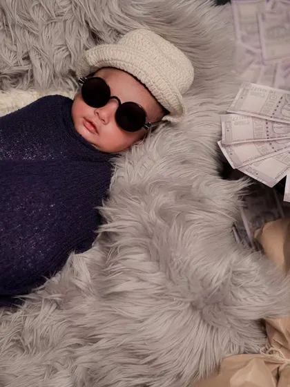 A fun and quirky "Money Heist" inspired theme for a newborn. Swaddled and wearing sunglasses, this little boss is surrounded by prop money for a playful shot.