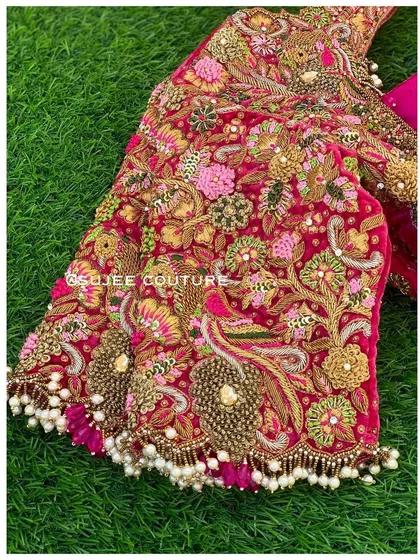 A close-up look at the rich texture and artistry of a velvet bridal blouse. The sleeve is densely covered in multi-tonal zardozi and knot work, featuring peacock motifs and finished with a delicate fringe of off-white pearls.