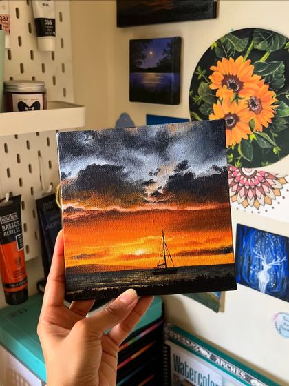The sailboat sunset painting held up against my studio wall, surrounded by other pieces of my art.