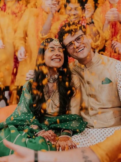 A joyful haldi ceremony photo, where the couple is showered with flower petals, and the bride's henna is visible.