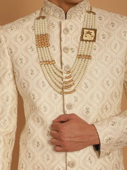 A close-up of the groom's accessory, a multi-layered pearl mala, which perfectly complements the ivory sherwani. We help you style your entire look, down to the last detail.