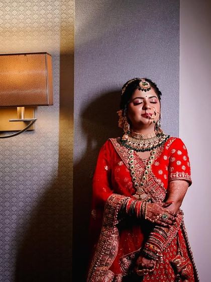 A full-length portrait of the bride in her stunning red lehenga. The dramatic side lighting creates a sophisticated and elegant look, highlighting the rich texture of her outfit. (Similar to 56)