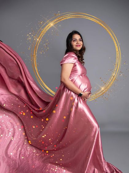 A beautiful solo portrait with a sparkling golden halo effect. The flowing pink satin gown catches the light perfectly, making the mom-to-be glow.