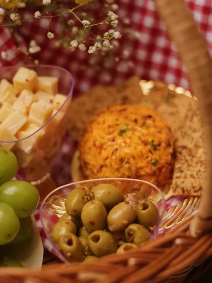 A close-up of the goodies inside our picnic basket. It includes a savory cheese dome, cheese cubes, olives, and crackers, all ready for you to enjoy.