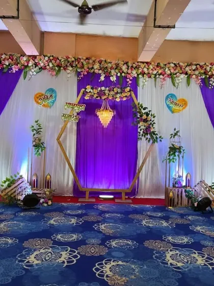 A royal-themed engagement stage with a purple and white color scheme. The hexagonal frame and chandelier add a touch of grandeur to the decor.