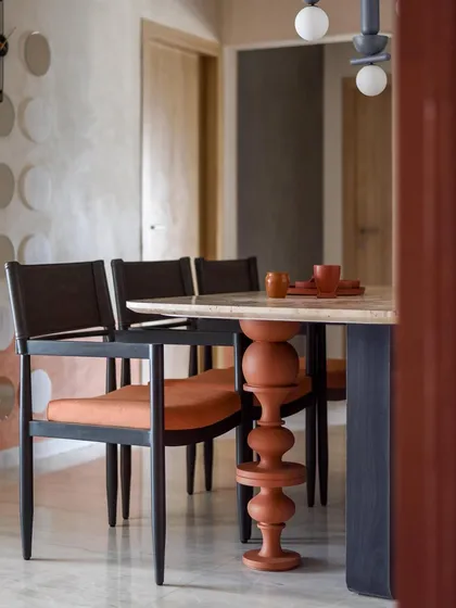 A close-up of the dining table's unique turned wooden leg, painted in a rich terracotta hue. This whimsical detail adds a playful touch to the space.
